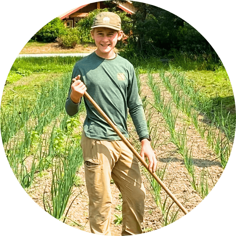 Child smiling and holding a rake in the onion field at Ice Cap Organics certified organic farm in Pemberton BC